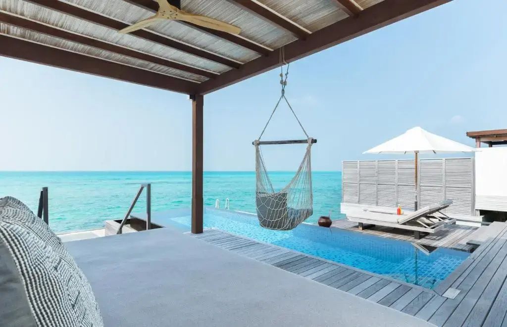 Holzdeck mit Hängesessel und kleinem Pool mit Blick auf das blaue Meer.
