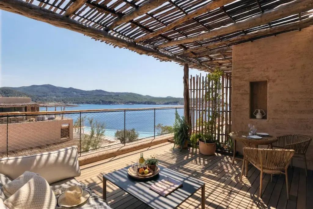 Überdachte Holzterrasse mit Blick auf eine Bucht und die hügelige Küstenlandschaft.