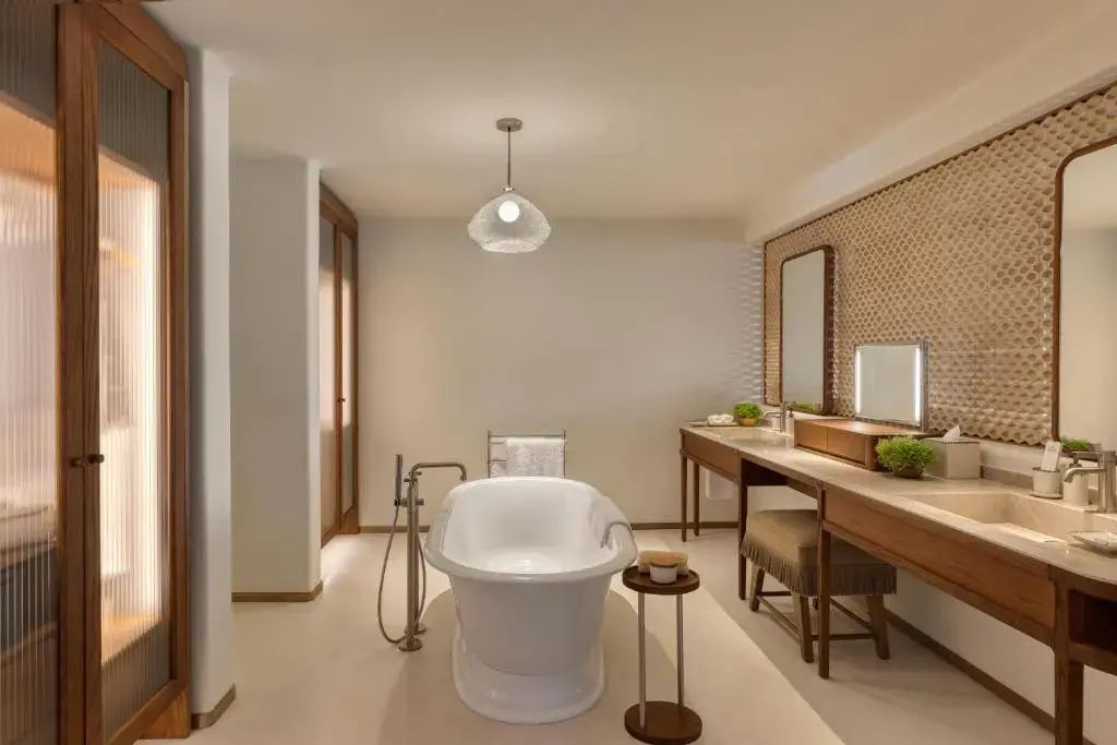 Helles Badezimmer mit freistehender Badewanne und großem Holzwaschtisch mit Spiegeln.
