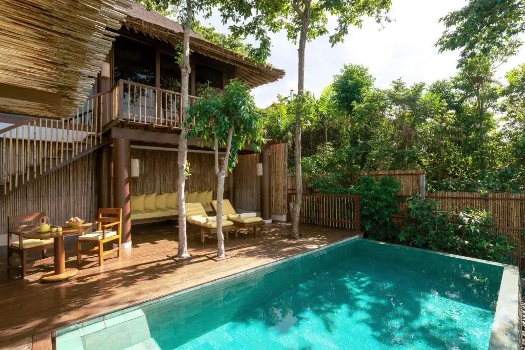 Holzdeck einer Villa mit kleinem Swimmingpool, Sonnenliegen und dichtem Grün.