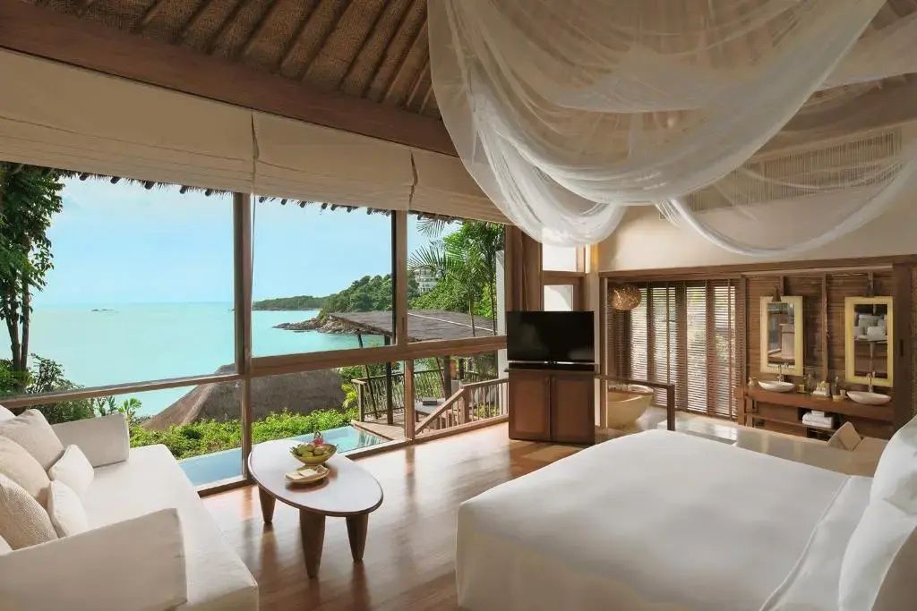 Helles Schlafzimmer mit Doppelbett, Moskitonetz und großen Fenstern mit Blick auf das Meer und die Küste.