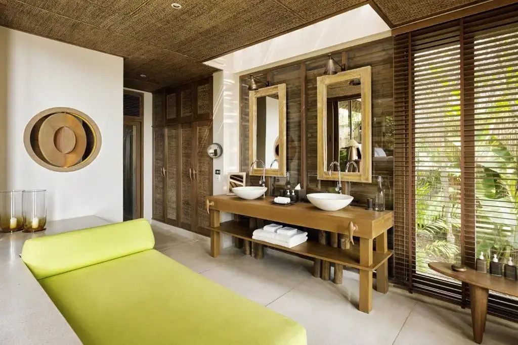 Badezimmer mit Doppelwaschtisch aus Holz, zwei runden Waschbecken und einer grünen Liege.