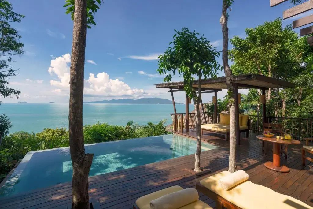 Pool auf einer Holzterrasse mit Liegestühlen und freiem Blick auf das blaue Meer.