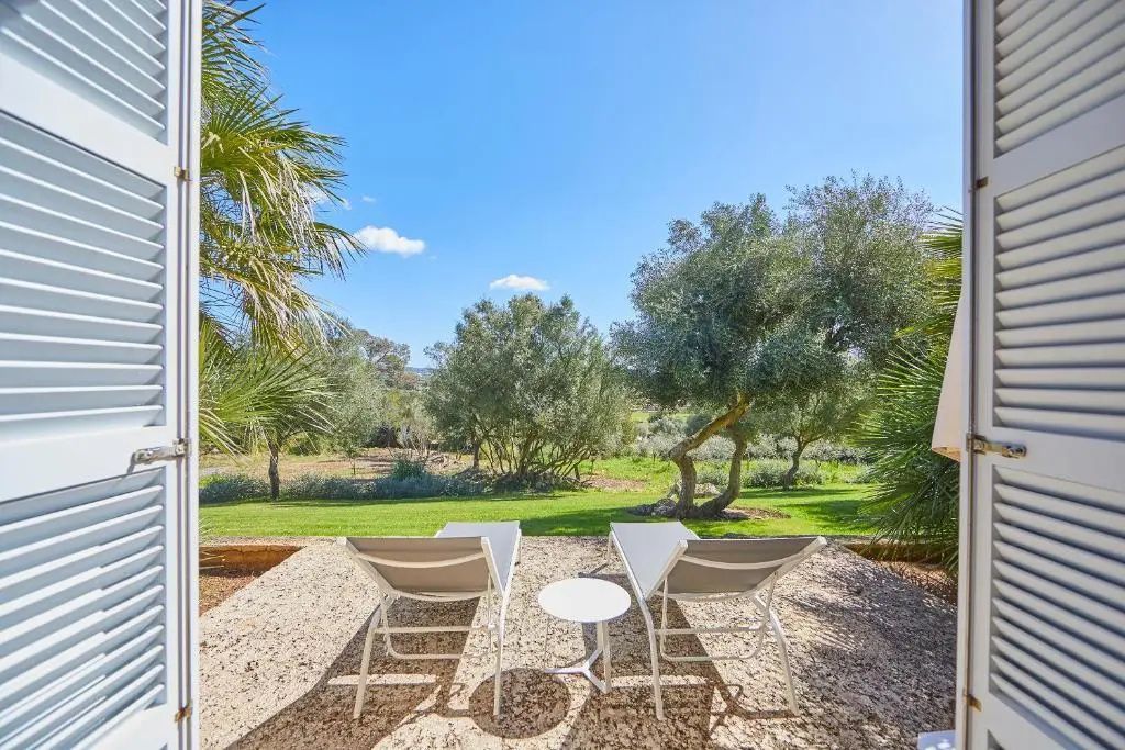 Zwei weiße Sonnenliegen auf einer Terrasse mit Blick auf den grünen Garten.