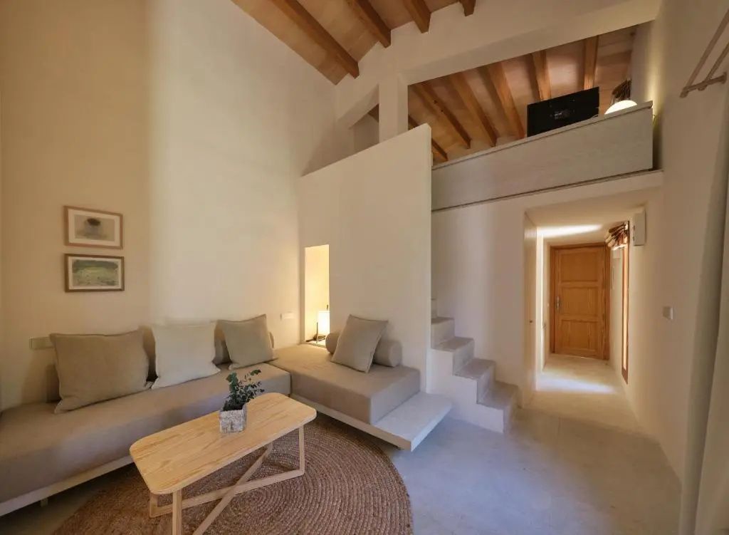Modern eingerichteter Wohnbereich mit hellem Sofa, Holzcouchtisch und Treppe zur Empore.