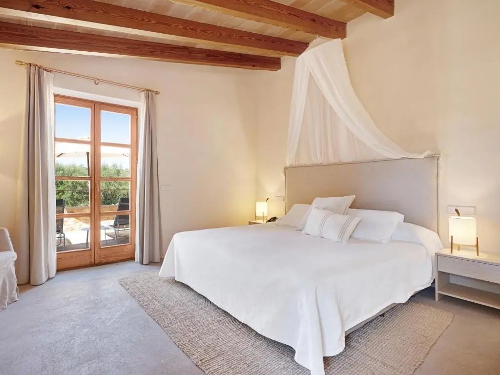 Helles Hotelzimmer mit großem Doppelbett, Baldachin, Holzbalkendecke und Balkontür zur Terrasse