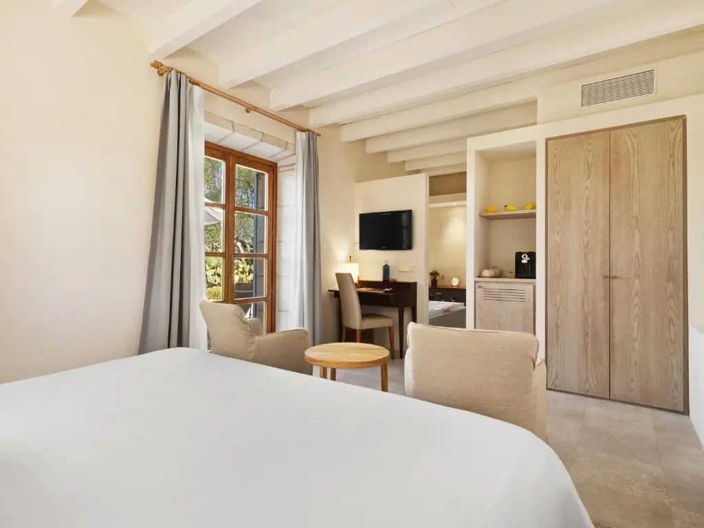 Wohnbereich im hellen Hotelzimmer mit zwei Sesseln, Schreibtisch und weißer Holzbalkendecke