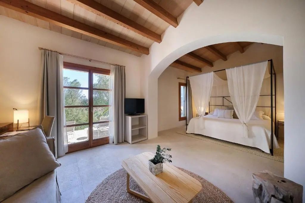 Helles Hotelzimmer mit Holzbalkendecke, einem Himmelbett und Zugang zur Terrasse.