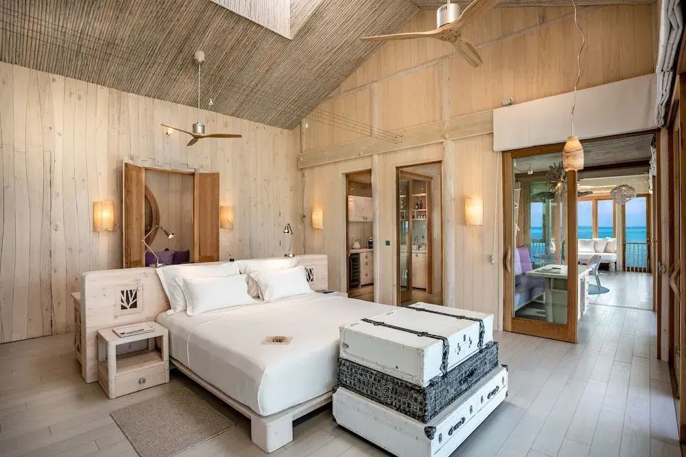 Helles Schlafzimmer aus Holz mit weißem Doppelbett und Deckenventilator.