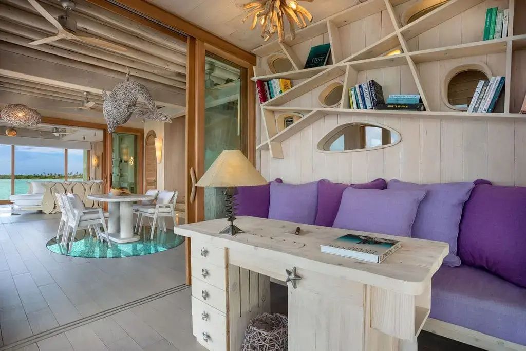 Wohnbereich aus Holz mit Schreibtisch, violettem Sofa und Wandregal.