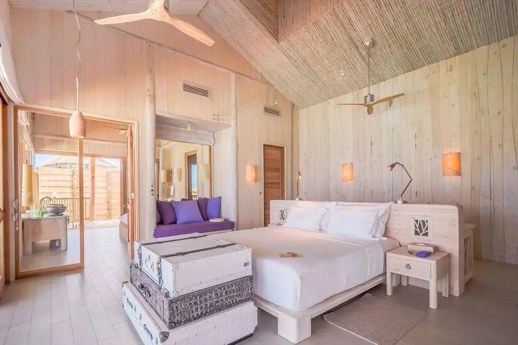 Helles Schlafzimmer aus Holz mit weißem Doppelbett und lila Sitznische.