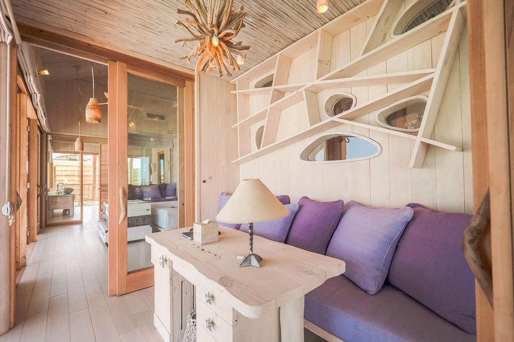 Arbeitsbereich im Zimmer mit Holzschreibtisch, Tischlampe und lila Sofa.