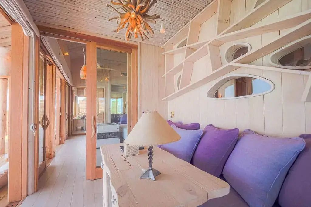 Wohnbereich einer Villa mit hellem Holz, lilafarbenen Sofakissen und einer Tischlampe.