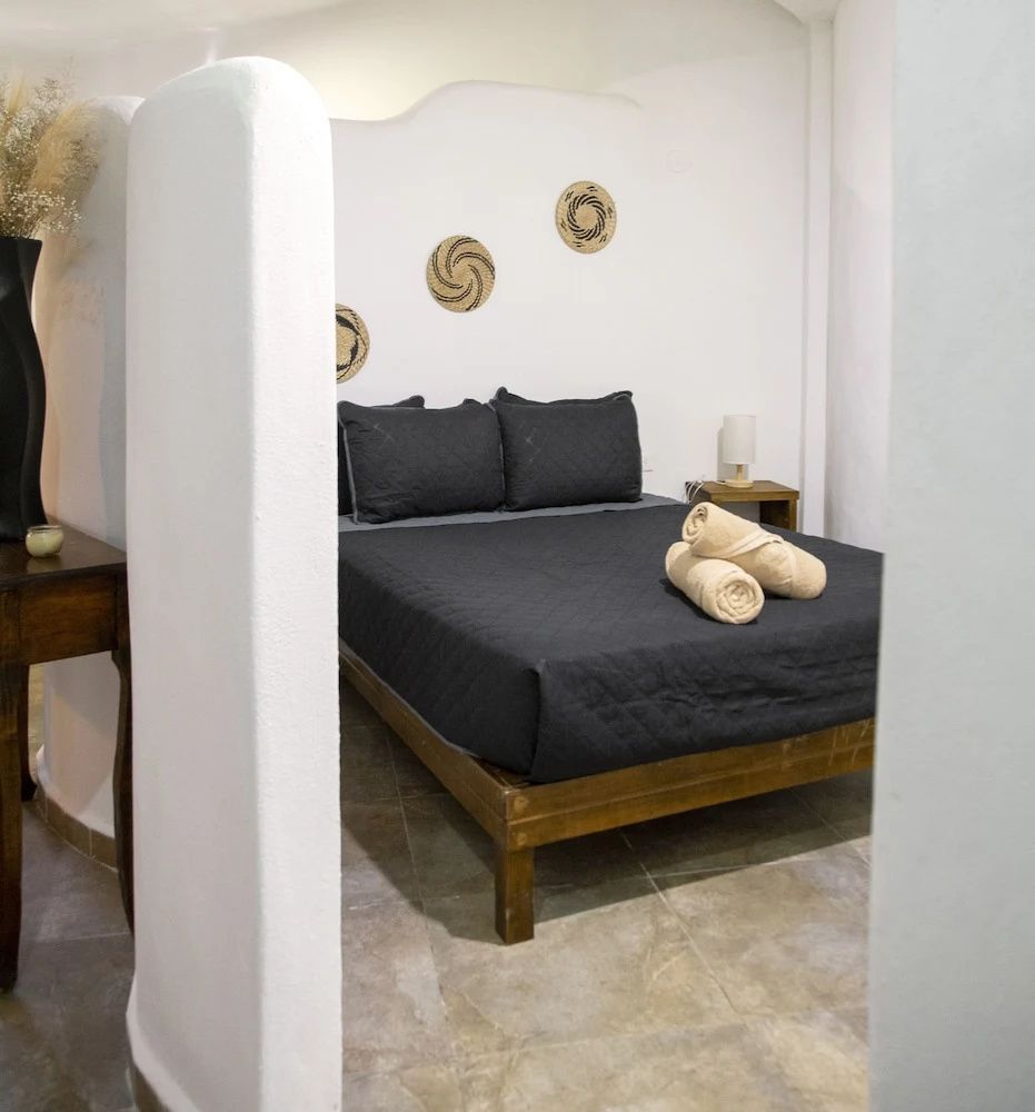 Ein Bett mit dunkler Tagesdecke und gerollten Handtüchern im hellen Zimmer.