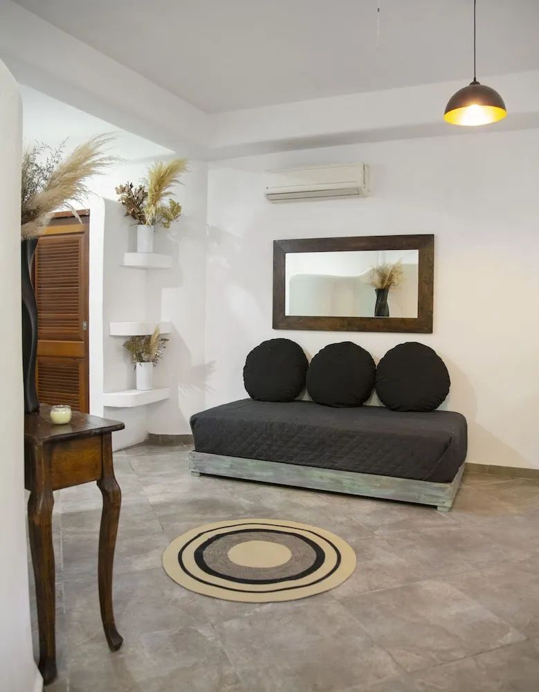 Wohnbereich mit dunkelgrauem Sofabett, kleinem Teppich und Holzspiegel an der Wand.