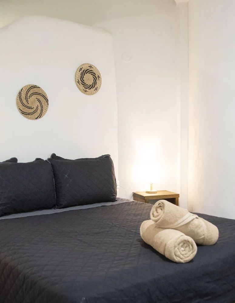 Doppelbett mit schwarzer Decke, eingerollten Handtüchern und geflochtener Wanddeko.