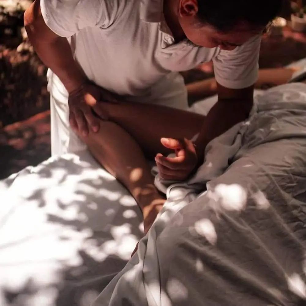 Ein Masseur führt eine Beinmassage bei einer auf der Liege liegenden Person durch.
