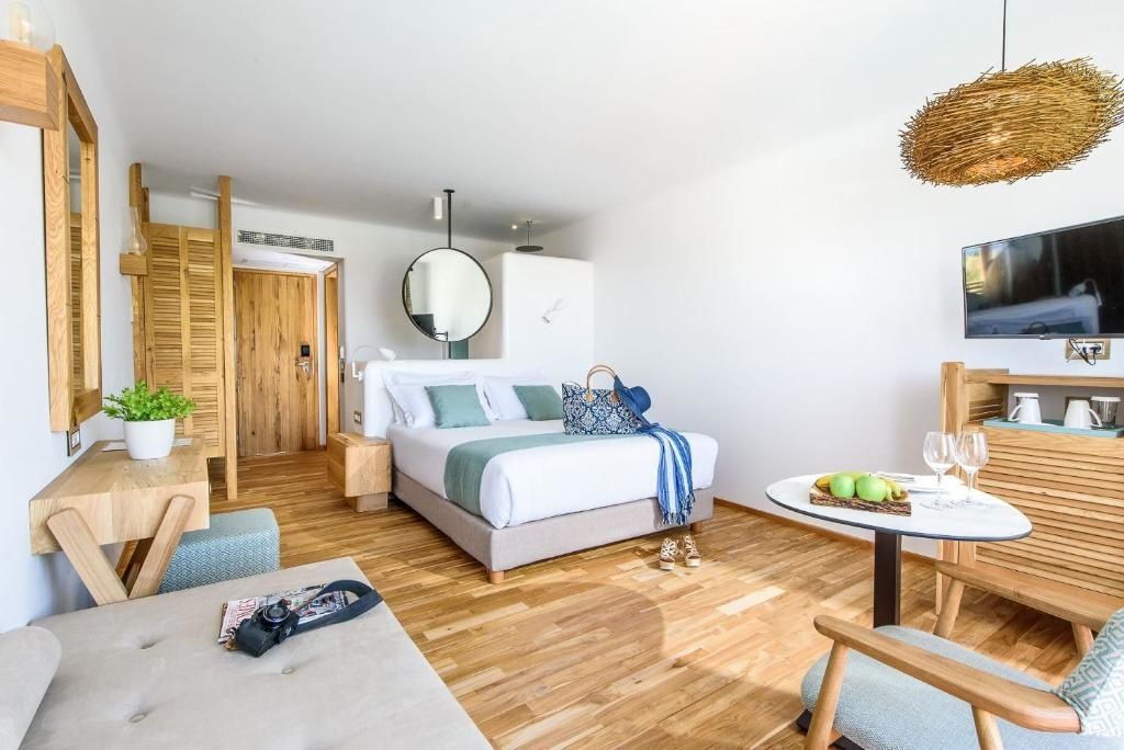 Helles Doppelzimmer mit Holzfußboden, weißem Bett und einem runden Spiegel über der Trennwand.