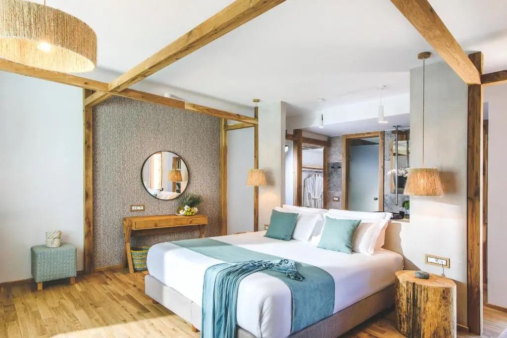 Doppelbett mit hellblauer Tagesdecke, Holzdeckenbalken und rundem Spiegel an der Wand.