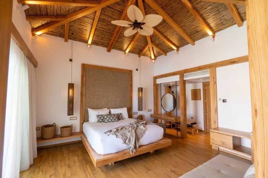 Hotelzimmer mit Holzdoppelbett, Strohdach-Decke und Holzdeckenventilator.