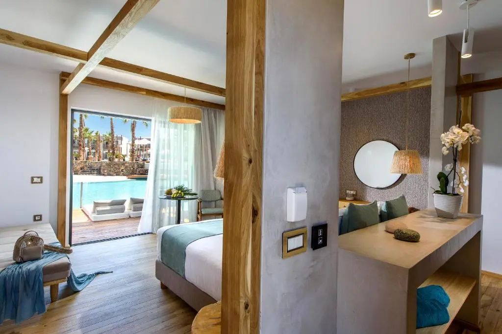 Hotelzimmer mit Doppelbett, Holzdekoration und Blick auf die Terrasse mit Pool.