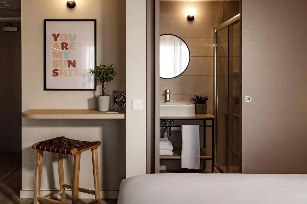 Sitzbereich im Hotelzimmer mit Holzhocker und Blick in das Badezimmer
