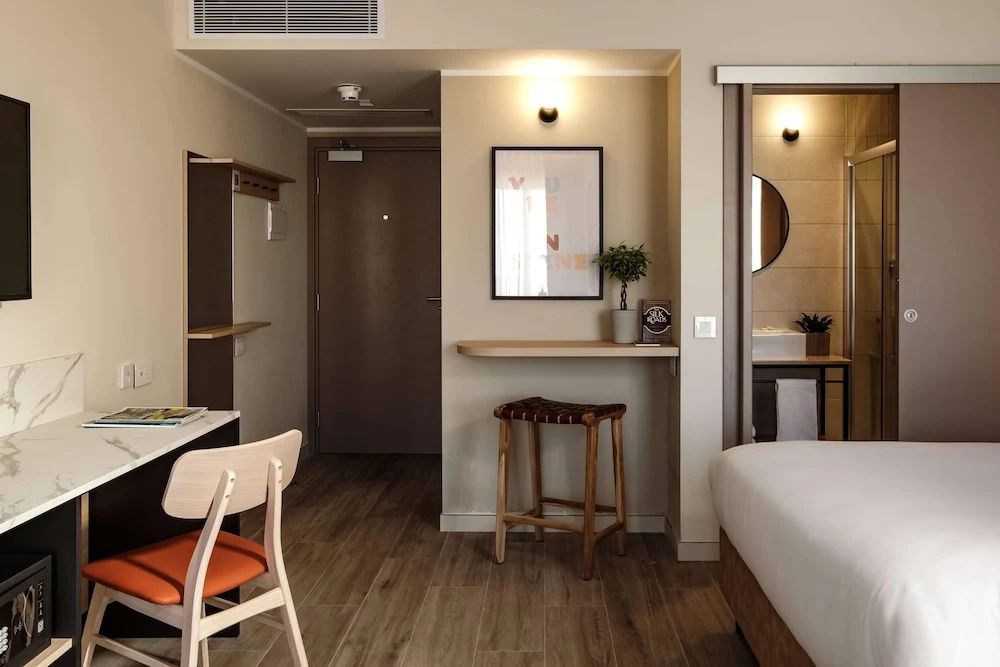Eingangsbereich des Zimmers mit kleiner Sitzgelegenheit und Blick in das Badezimmer.