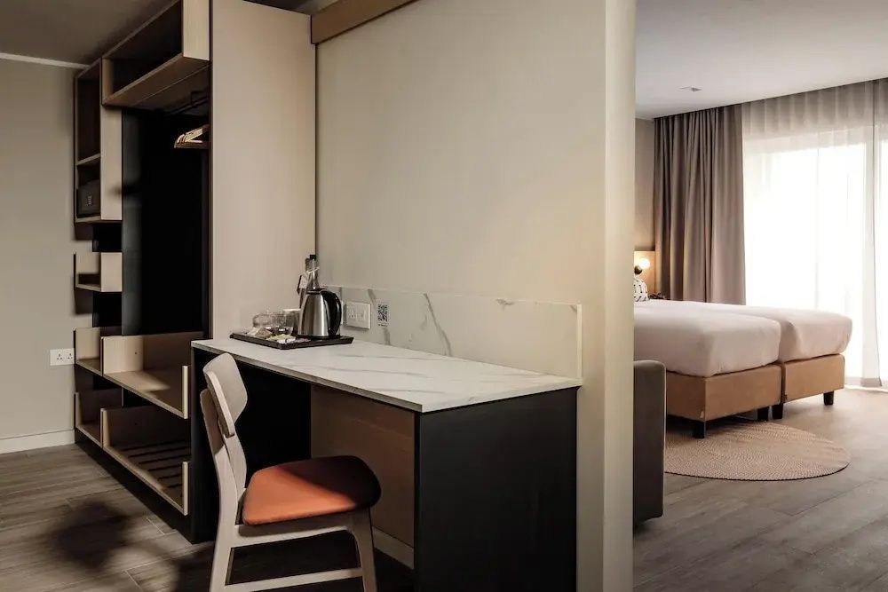 Schreibtischbereich im Hotelzimmer mit Stuhl, Wasserkocher und Blick auf das Doppelbett im Hintergrund.