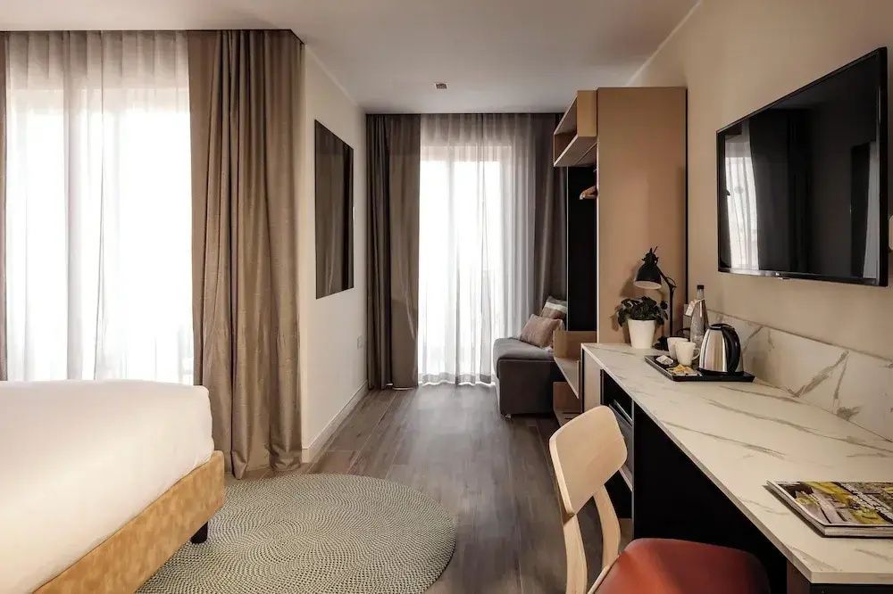 Helles Hotelzimmer mit Parkettboden, Schreibtisch und Zugang zum Balkon.