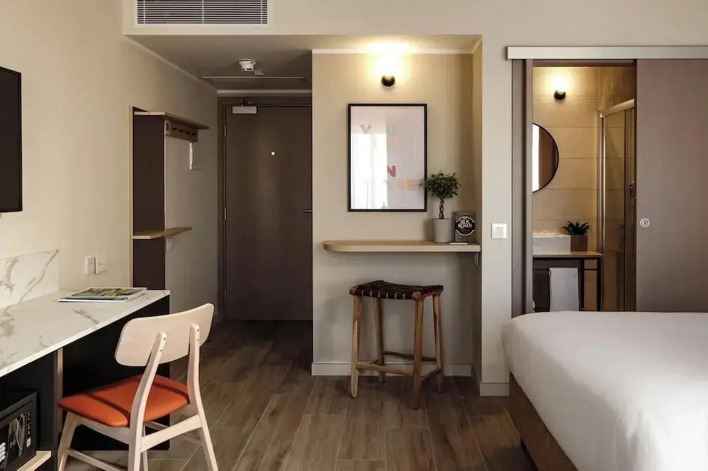Blick in ein modernes Hotelzimmer mit Sitzgelegenheiten, Holzfußboden und Durchgang zum Bad.