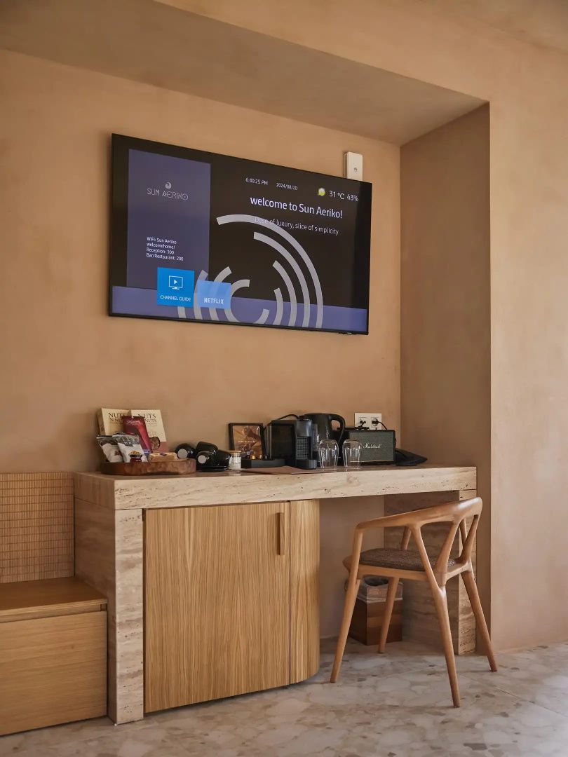 Schreibtisch aus Holz mit Stuhl, Kaffeezubehör und Flachbildfernseher an der Wand.