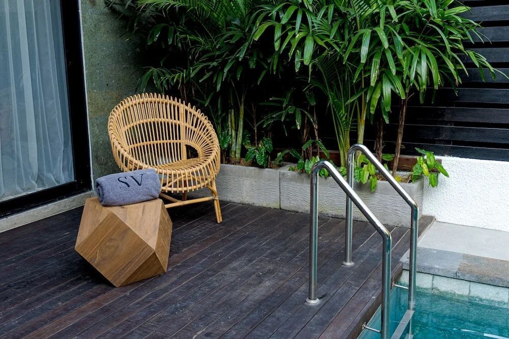 Rattansessel auf einer Holzterrasse am Pool umgeben von tropischen Pflanzen.