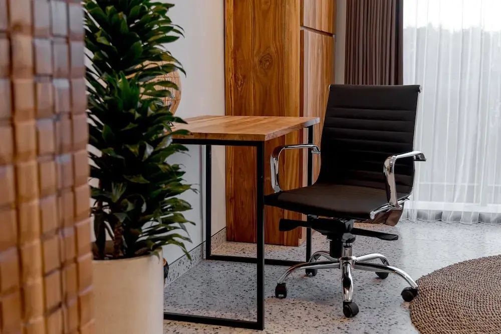 Schreibtisch aus Holz mit schwarzem Bürostuhl und einer Zimmerpflanze im Topf.