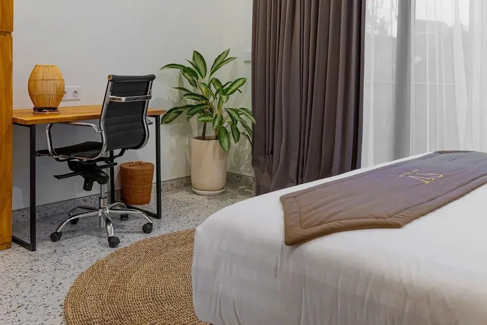 Schlafzimmerbereich mit Schreibtisch, Bürostuhl, Zimmerpflanze und weichem Doppelbett.