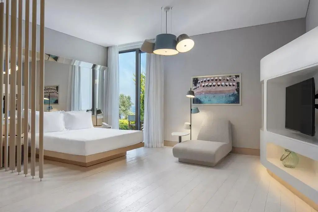 Modernes Hotelzimmer mit hellen Holzfussboeden, Doppelbett und Relaxsessel.