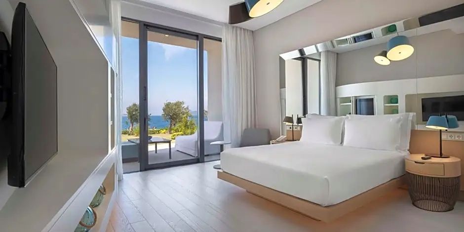 Helles Hotelzimmer mit großem Doppelbett und Glas-Schiebetür zur Terrasse mit Meerblick.
