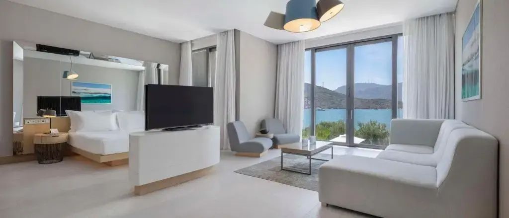 Wohnbereich einer Suite mit TV Möbel, zwei Sesseln und Blick auf das Meer.