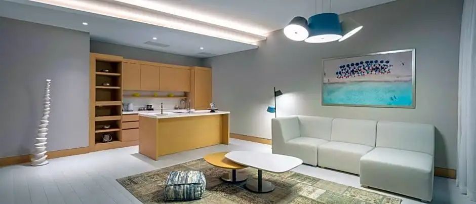 Offener Wohnbereich mit kleiner Küche, weißem Sofa und Couchtischen in einer Suite.