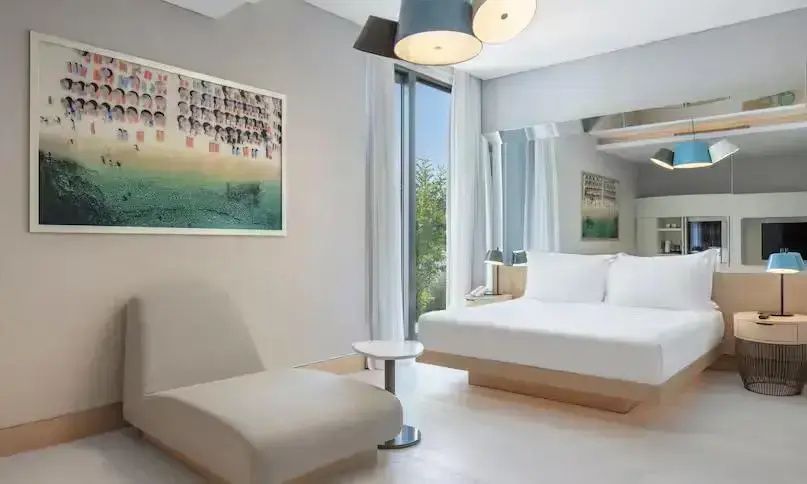 Modernes Schlafzimmer mit Doppelbett, Chaiselongue, modernem Gemälde an der Wand und hellem Holzboden.