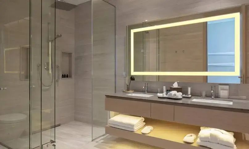Badezimmer mit Doppelwaschtisch, beleuchtetem Spiegel und einer verglasten Dusche.