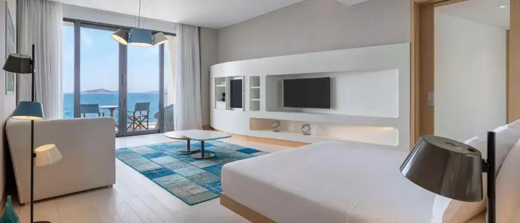 Hotelzimmer mit Bett, blauem Teppich, weißer Schrankwand und Zugang zum Balkon.