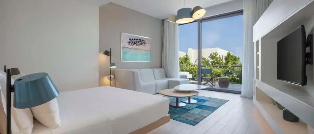 Helles Hotelzimmer mit weisser Eckcouch, Couchtisch und Blick auf die Terrasse.