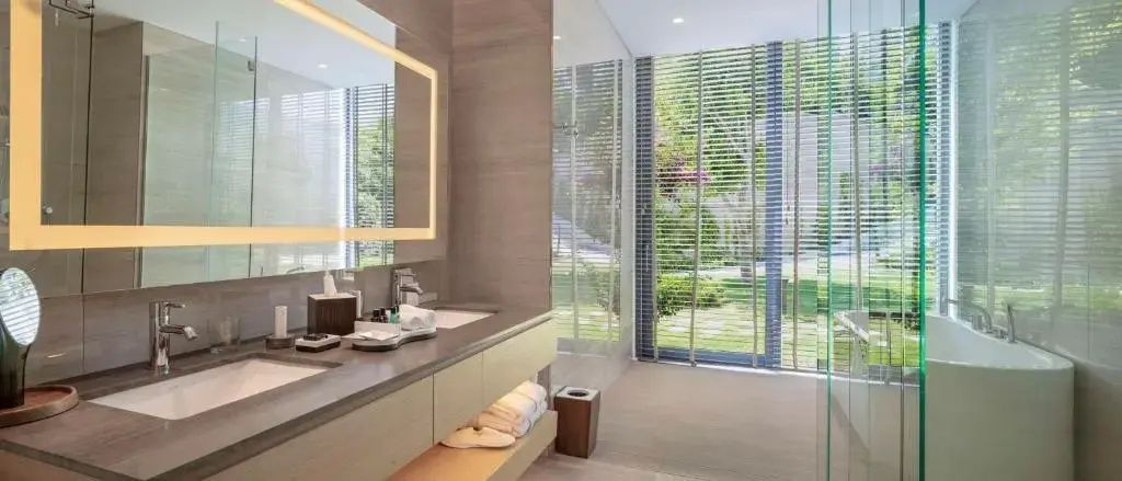 Badezimmer mit beleuchtetem Spiegel, Waschtisch und bodentiefen Fenstern.
