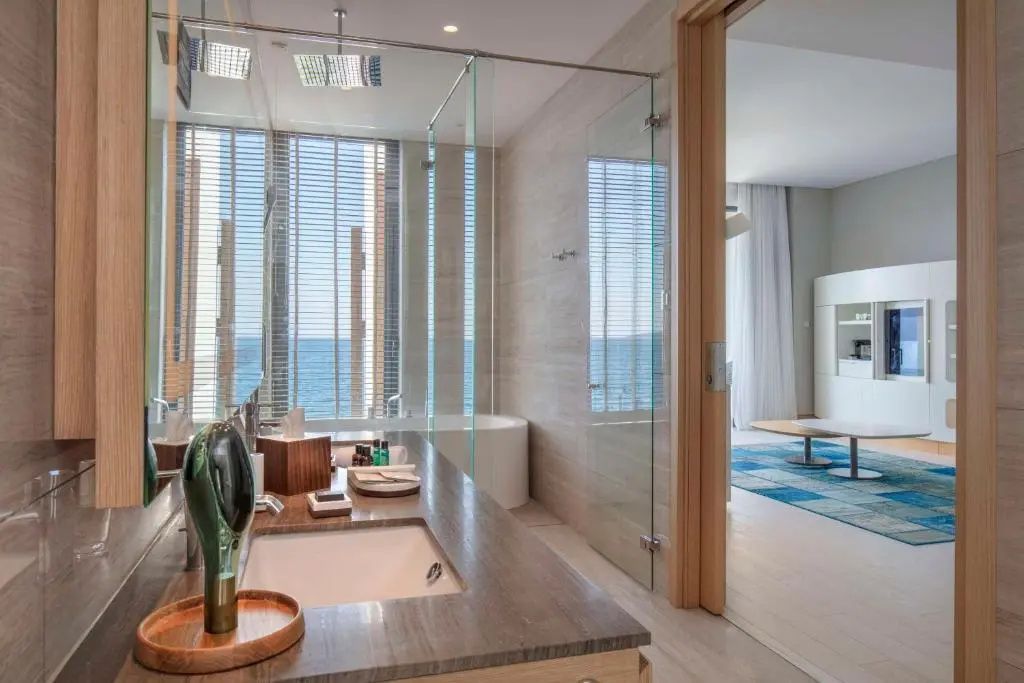 Badezimmer mit Waschtisch, freistehender Badewanne und Glasdusche vor dem Fenster.