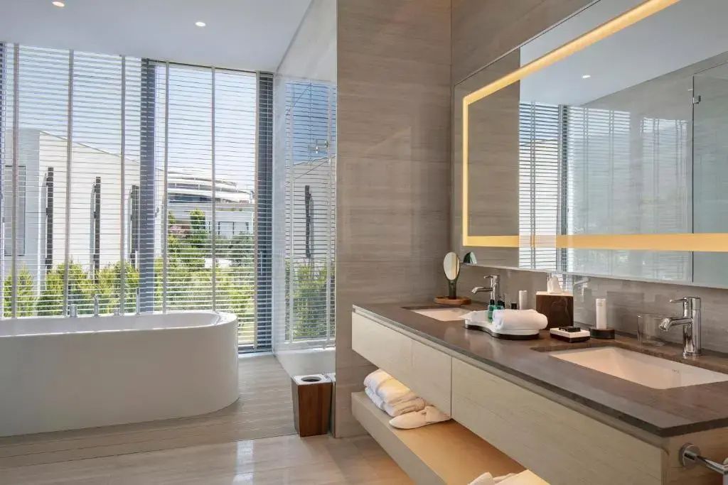 Badezimmer mit großer Badewanne vor bodentiefem Fenster und Holzwaschtisch.