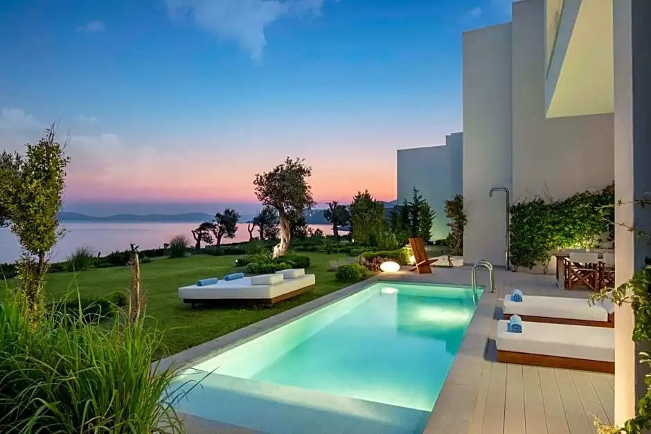 Privatpool auf einer Terrasse neben einer Rasenfläche mit Sonnenliegen und Blick auf das Meer bei Dämmerung.