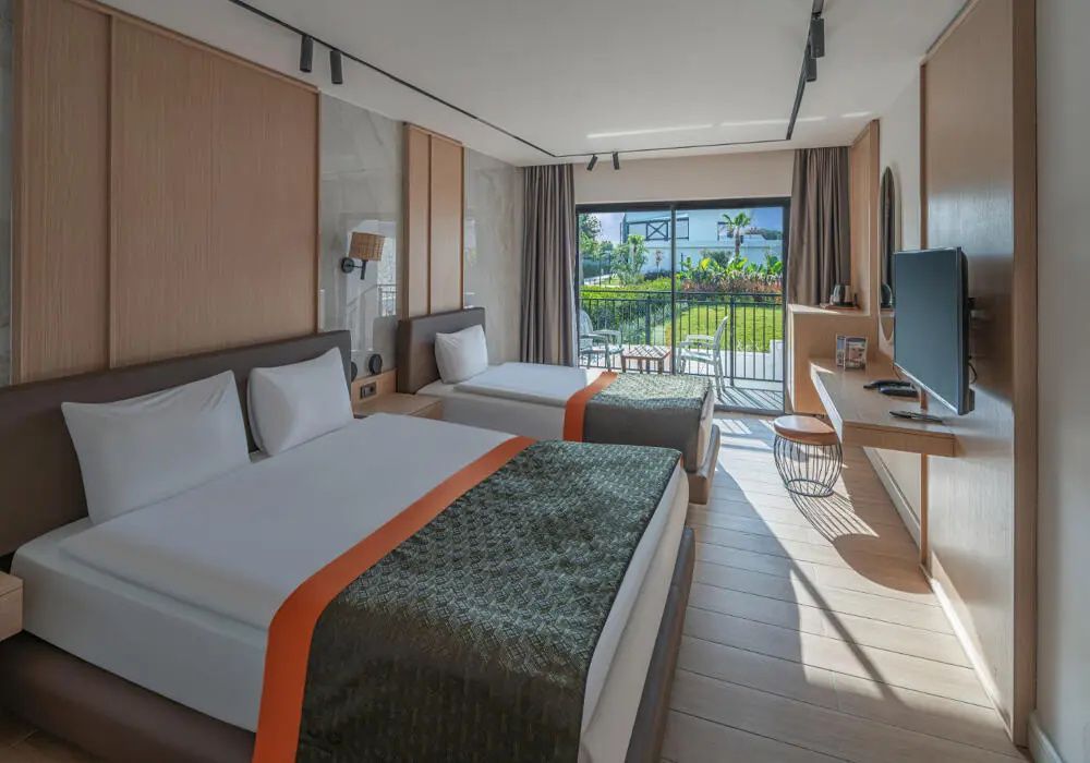 Modernes Hotelzimmer mit zwei Betten, Holzfußboden und Balkonzugang mit Blick ins Grüne.