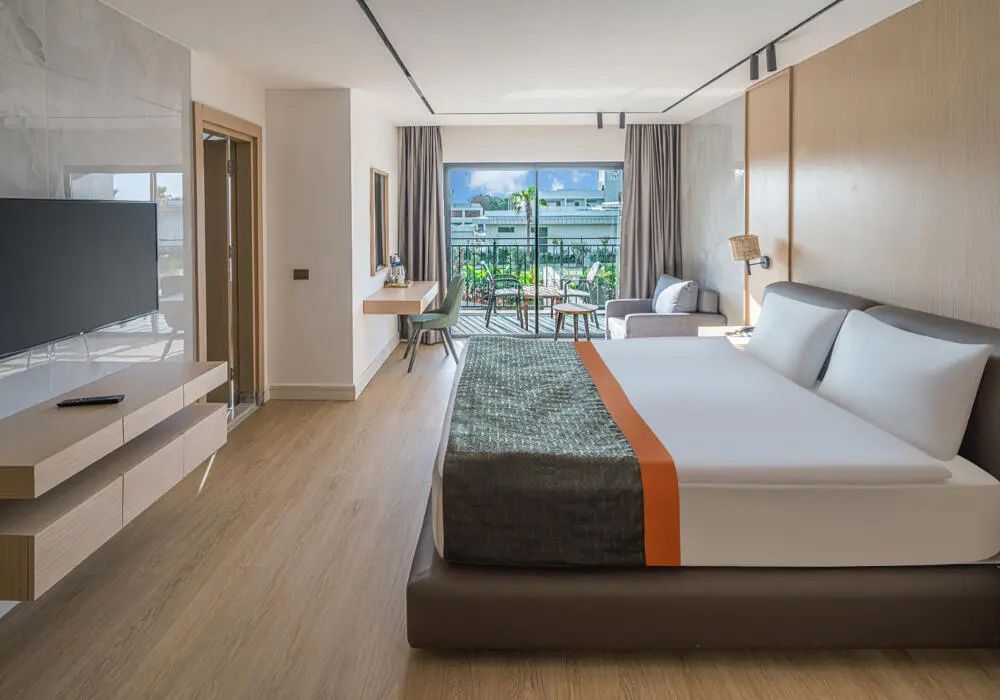 Hell eingerichtetes Schlafzimmer mit Doppelbett, Schreibtisch und Balkon mit Blick auf den Garten.