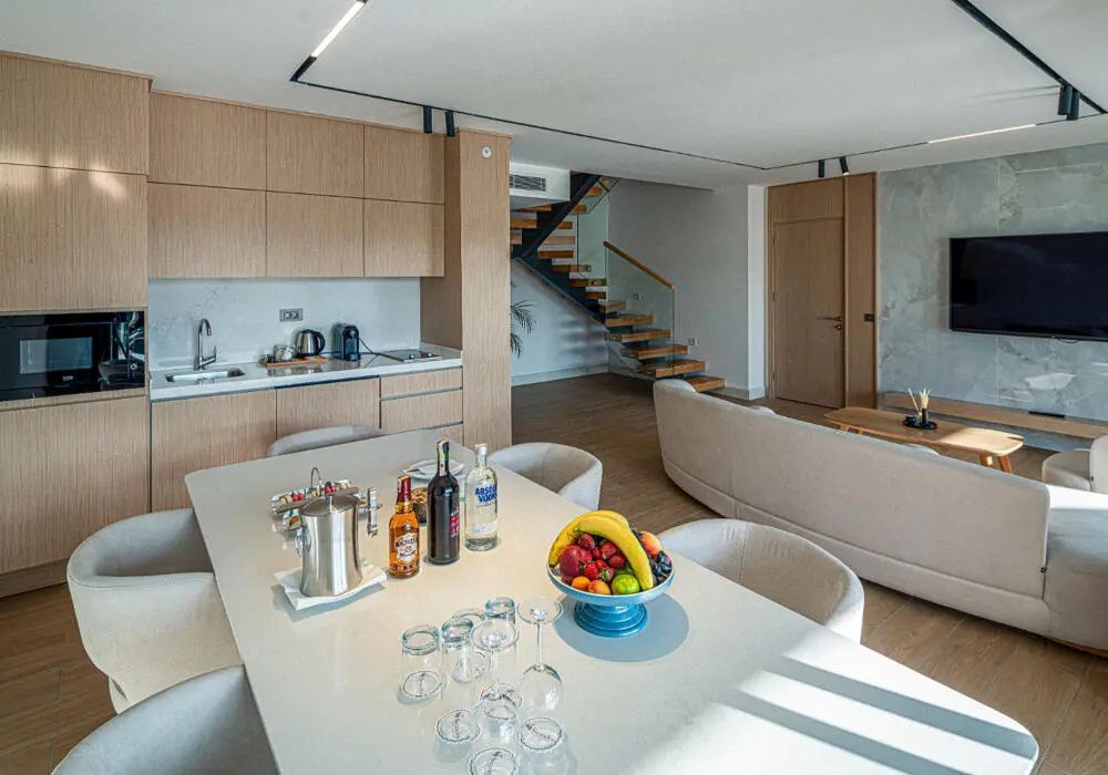Geräumiges Wohnzimmer einer Suite mit Esstisch, Küchenzeile und Holztreppe ins obere Stockwerk.
