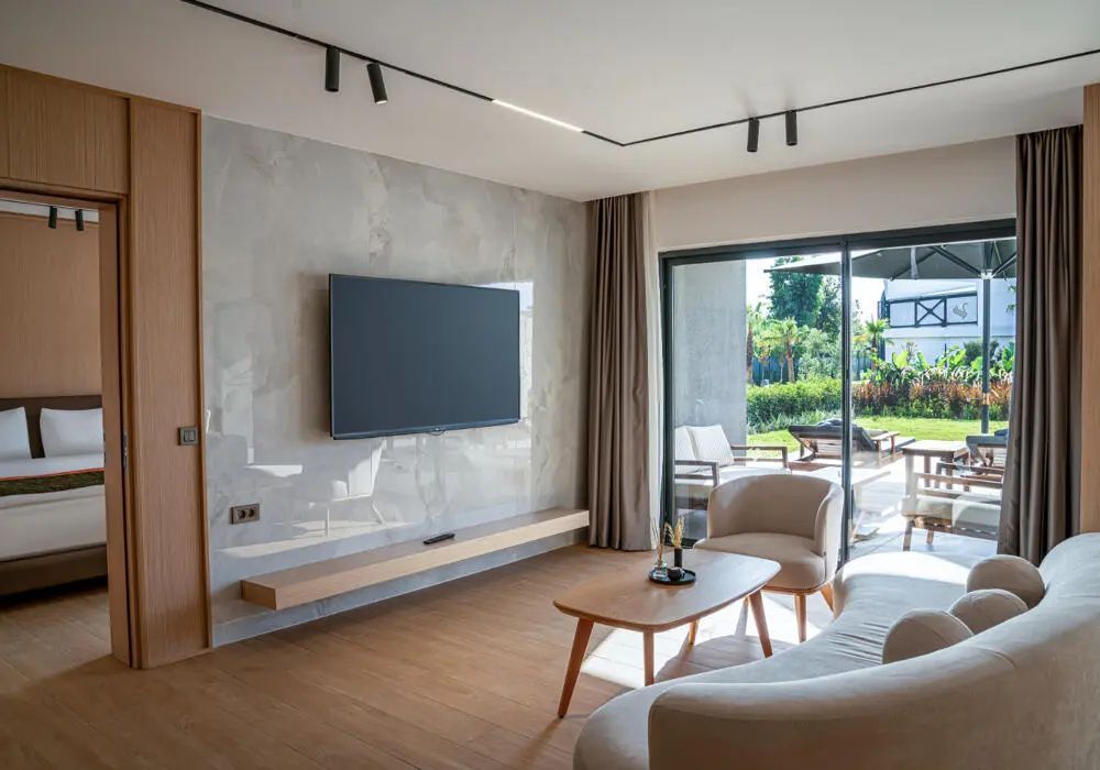 Wohnbereich mit Flachbild TV an der Wand, Couch, Couchtisch und Zugang zur Terrasse im Erdgeschoss.
